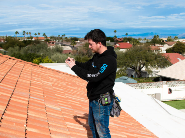 A roof inspector of Axis Roofing on a tile roof taking photos of damages in Fountain Hills, Arizona